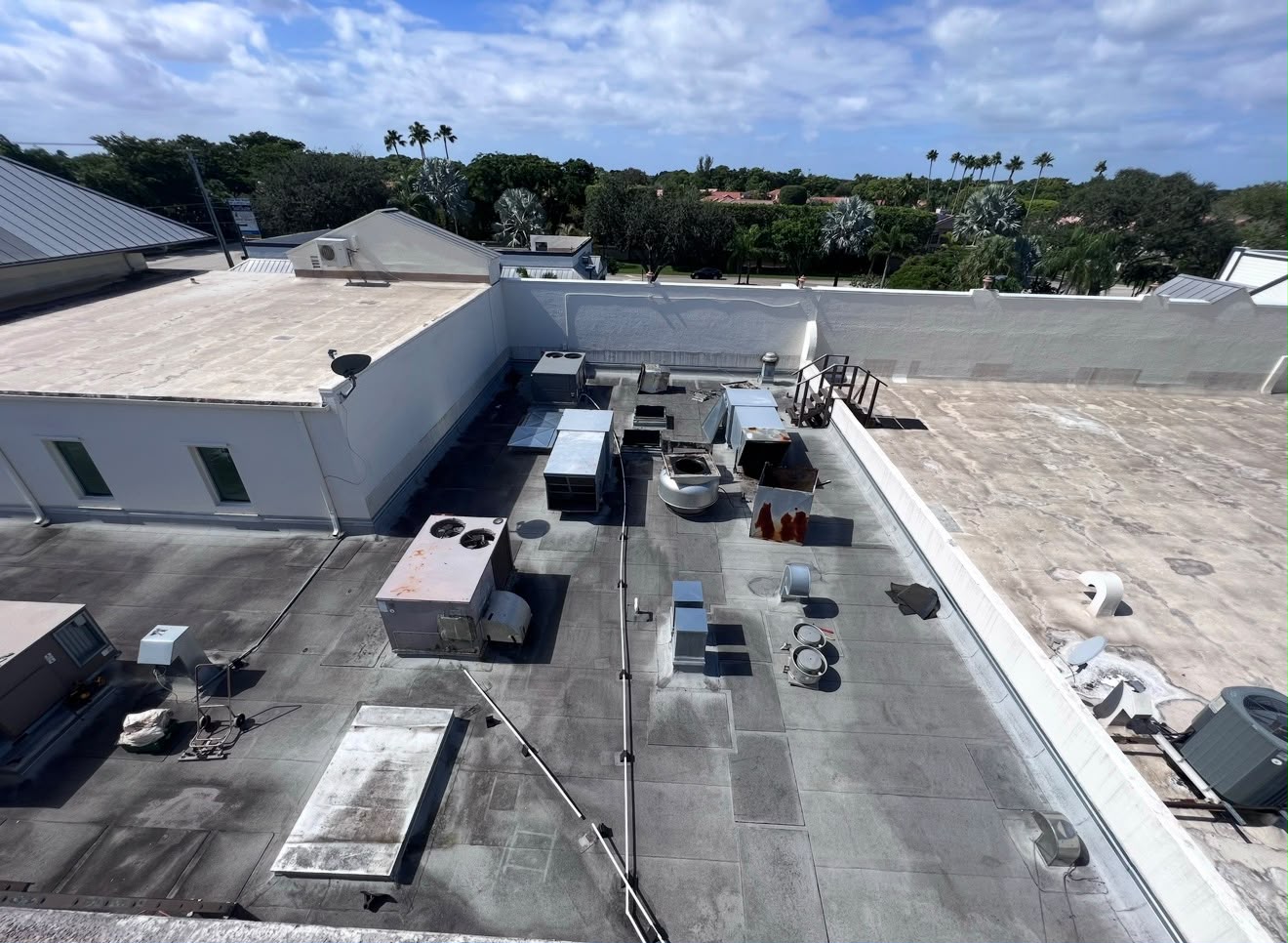 Before — A commercial roof carrying rooftop HVAC, ducting and equipment stands. The coating is carried up the parapets and detailed around every curb.