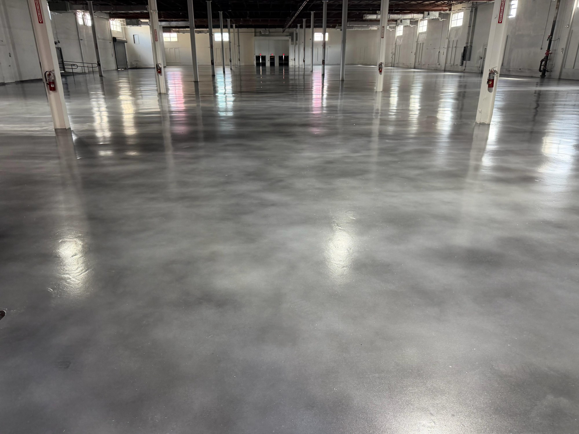 Finished — The same warehouse floor part-way through and completed — ground back, densified and burnished between the standing columns.